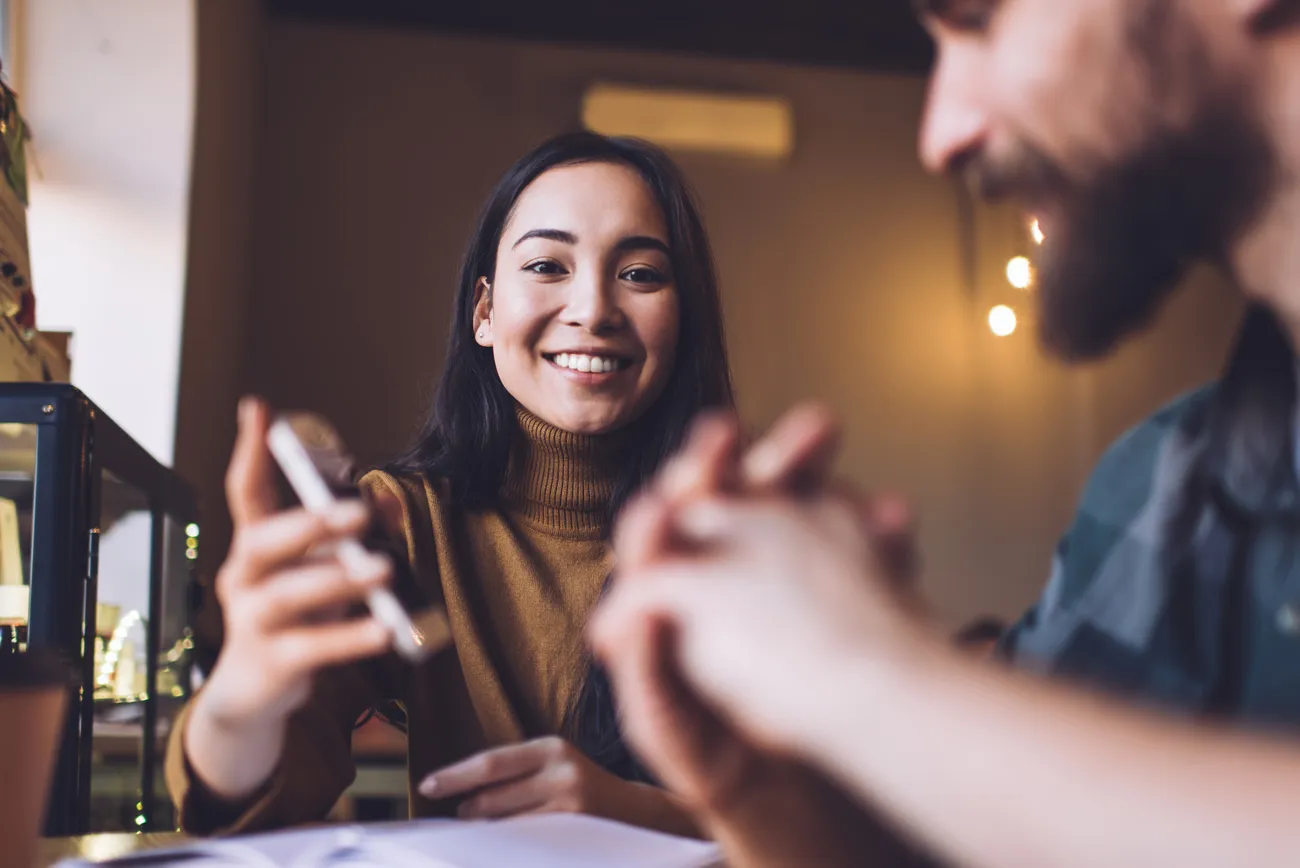 Two people talking across a café table, one holding a phone
